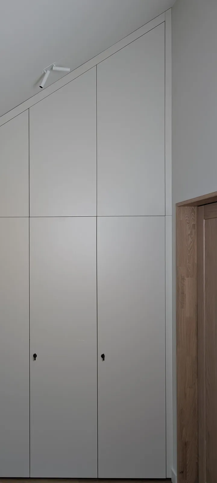 Hvit garderobe under skråtak med høye dører og små knotter, tilpasset takvinkelen
